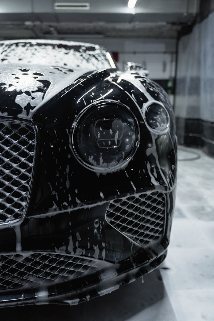 portfolio-05 Close-up of a sleek black luxury car with soapy foam during a carwash process.